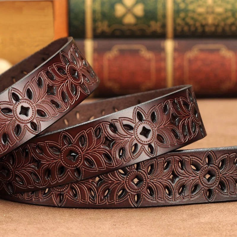 Brown leather belt with intricate floral patterns on a wooden surface.